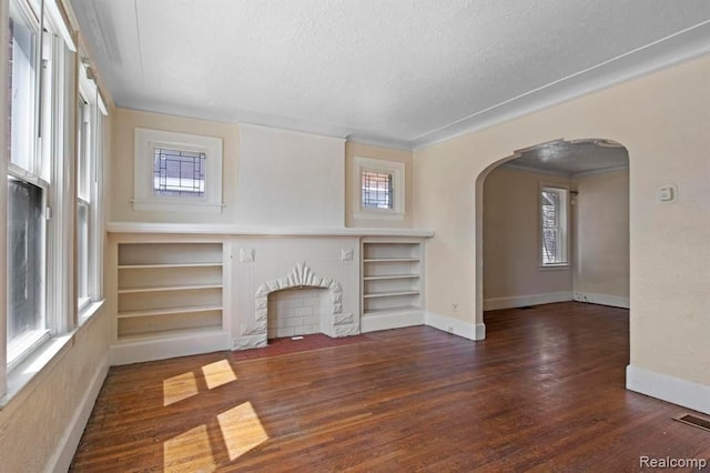 unfurnished living room featuring baseboards, a textured ceiling, arched walkways, and wood finished floors