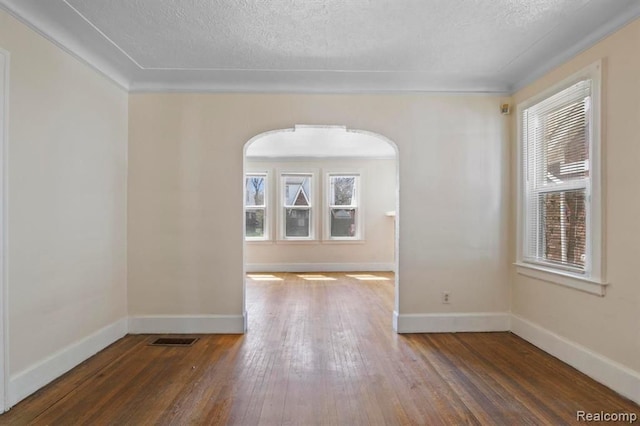 empty room featuring wood-type flooring, visible vents, arched walkways, and baseboards