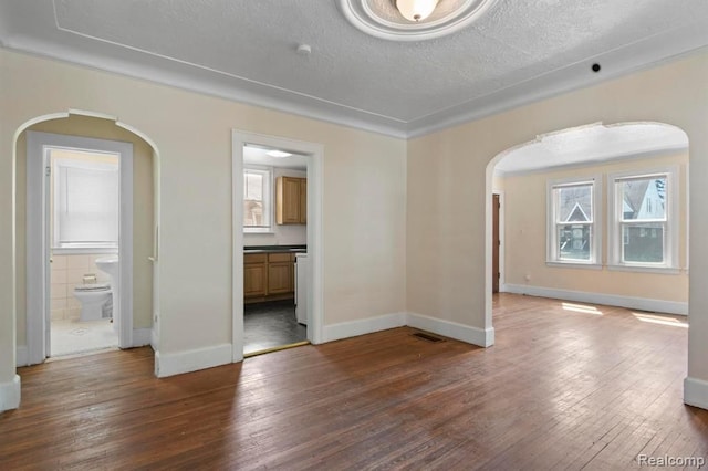 spare room featuring hardwood / wood-style flooring, baseboards, arched walkways, and a textured ceiling