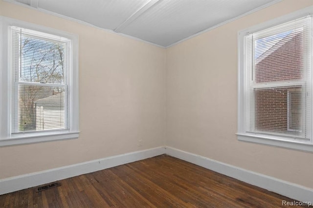 empty room featuring visible vents, baseboards, dark wood-type flooring, and ornamental molding