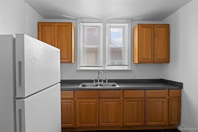 kitchen featuring brown cabinetry, freestanding refrigerator, a sink, and dark countertops