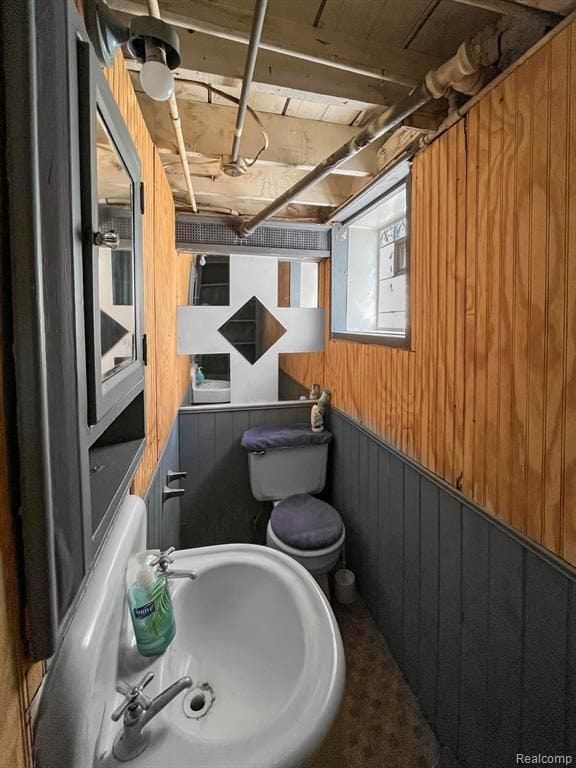 bathroom featuring toilet, wooden walls, and a sink