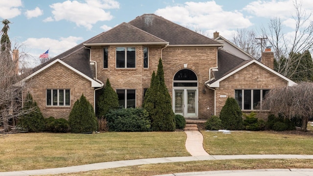 traditional-style home with roof with shingles, a front lawn, french doors, and brick siding