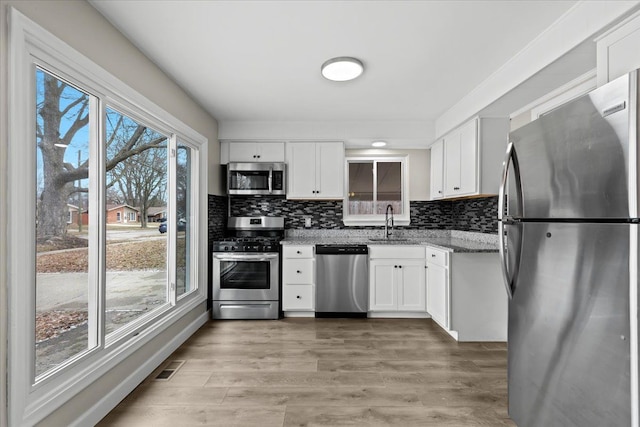 kitchen featuring light stone counters, stainless steel appliances, white cabinetry, a sink, and light wood-type flooring