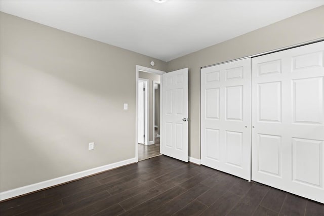 unfurnished bedroom with dark wood-style flooring, a closet, and baseboards