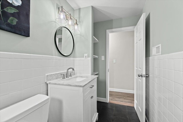 half bath with a wainscoted wall, tile walls, toilet, vanity, and tile patterned flooring