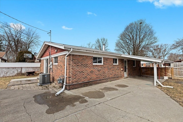 rear view of house with driveway, central AC unit, an attached carport, fence, and brick siding