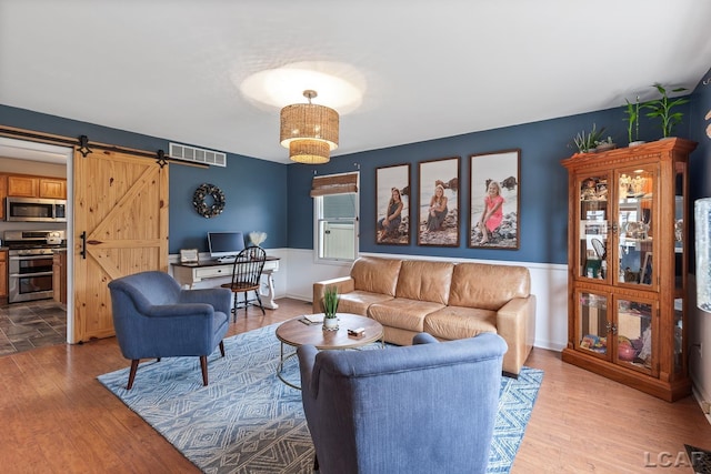 living area with wood finished floors, visible vents, baseboards, and a barn door