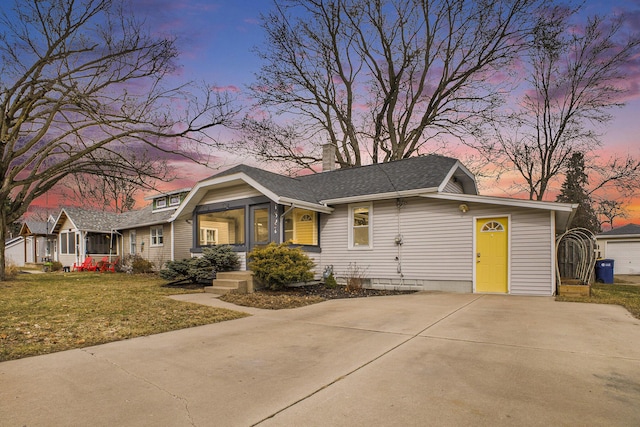 view of front of house with a chimney, driveway, roof with shingles, and a front yard