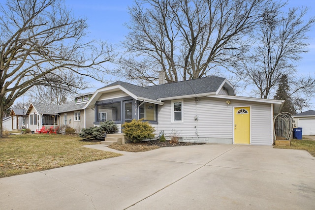 view of front of property with a chimney, a shingled roof, concrete driveway, a front yard, and a sunroom