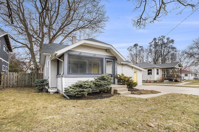 view of front facade with concrete driveway, fence, a chimney, and a front lawn