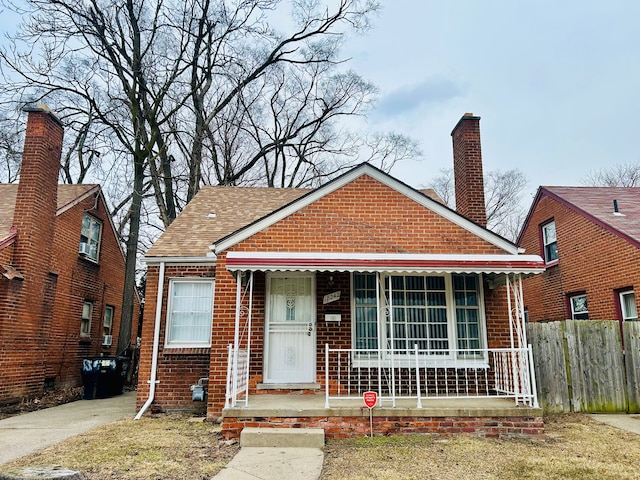 bungalow with a porch, a chimney, fence, and brick siding