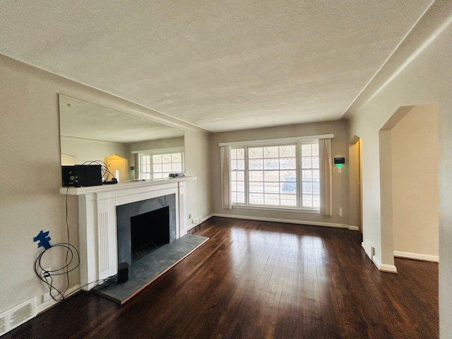 unfurnished living room with baseboards, visible vents, a fireplace with raised hearth, dark wood-style flooring, and a textured ceiling