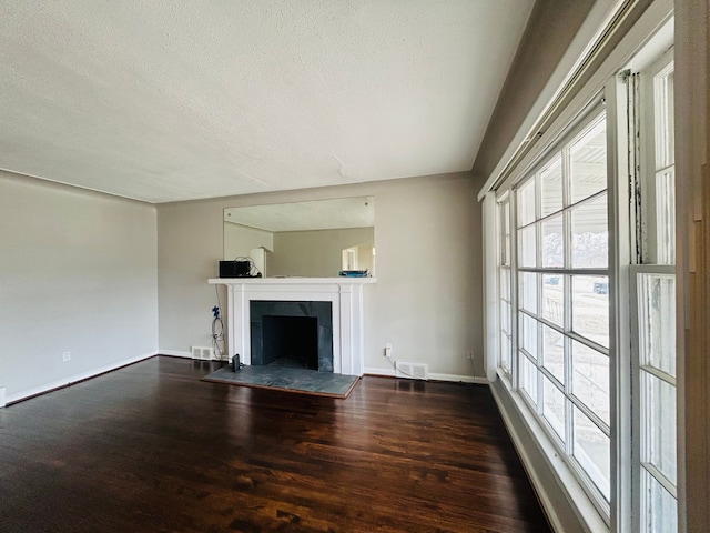 unfurnished living room with visible vents, baseboards, dark wood finished floors, a tiled fireplace, and a textured ceiling