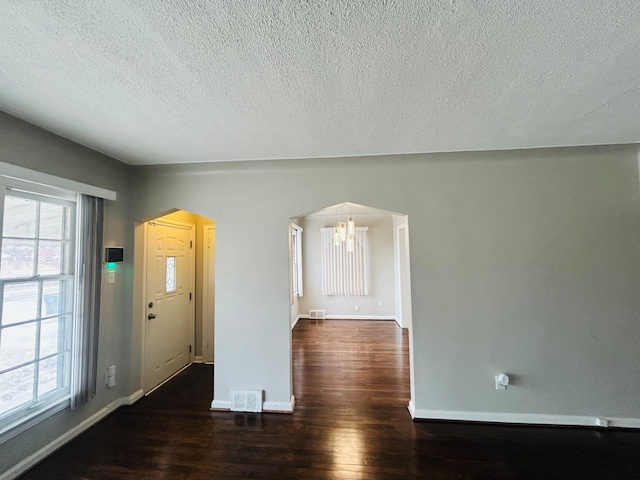 entrance foyer featuring arched walkways, dark wood-style flooring, visible vents, and plenty of natural light