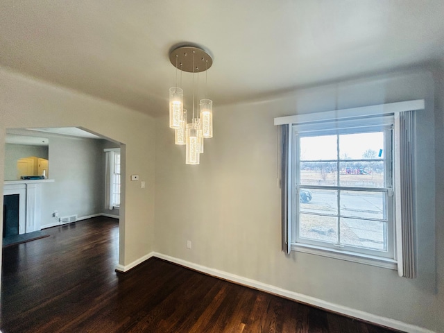 unfurnished dining area featuring a healthy amount of sunlight, dark wood-style floors, arched walkways, and a fireplace with raised hearth