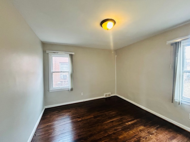 unfurnished room featuring dark wood-type flooring, a wealth of natural light, visible vents, and baseboards