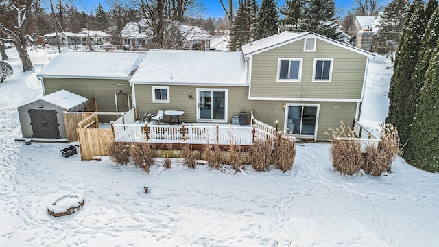 snow covered rear of property with a storage shed, an outdoor structure, and a wooden deck