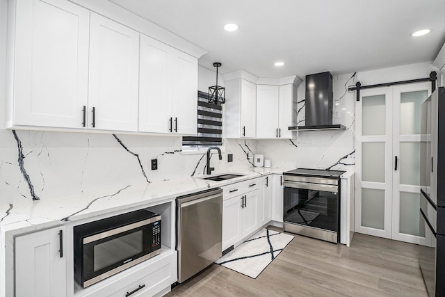 kitchen with a sink, white cabinetry, light wood-style floors, wall chimney range hood, and appliances with stainless steel finishes