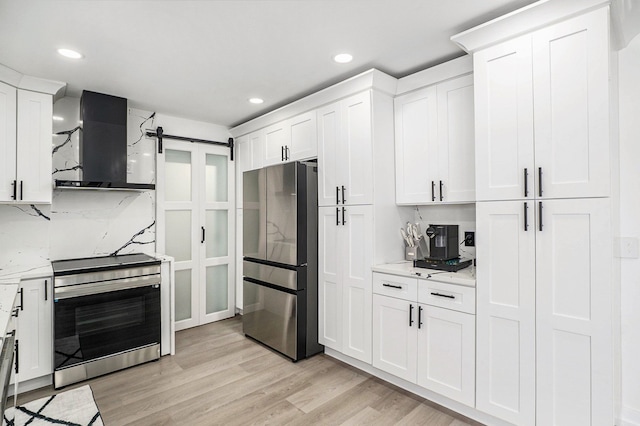 kitchen featuring a barn door, white cabinets, wall chimney exhaust hood, appliances with stainless steel finishes, and light wood-style floors