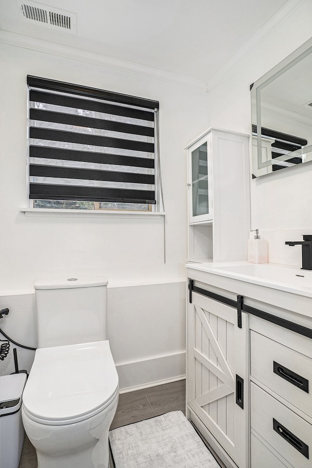 bathroom featuring toilet, wood finished floors, vanity, visible vents, and ornamental molding