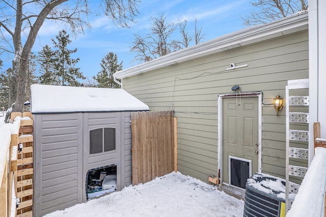 snow covered patio with central air condition unit, fence, and an outdoor structure