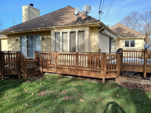 back of property with a deck, roof with shingles, a yard, and a chimney