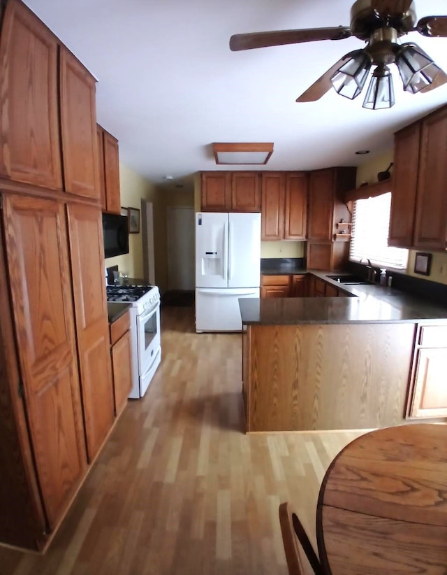 kitchen featuring a peninsula, white appliances, a sink, light wood finished floors, and dark countertops