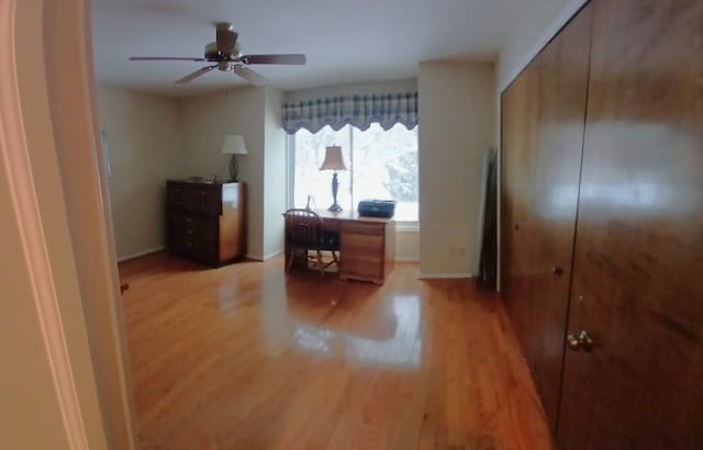 office area with light wood-type flooring, ceiling fan, and baseboards