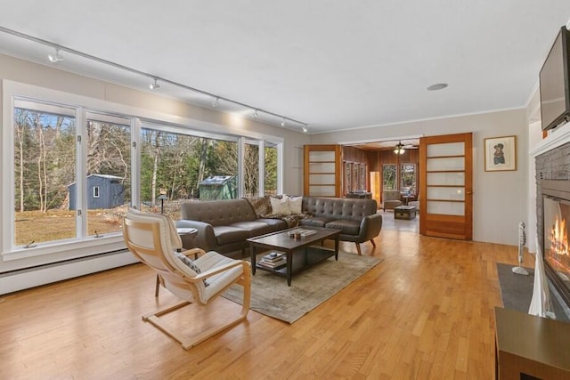 living area with ornamental molding, wood finished floors, a fireplace with flush hearth, and a healthy amount of sunlight