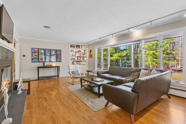 living area with a baseboard heating unit, built in shelves, a fireplace with flush hearth, and light wood-style floors