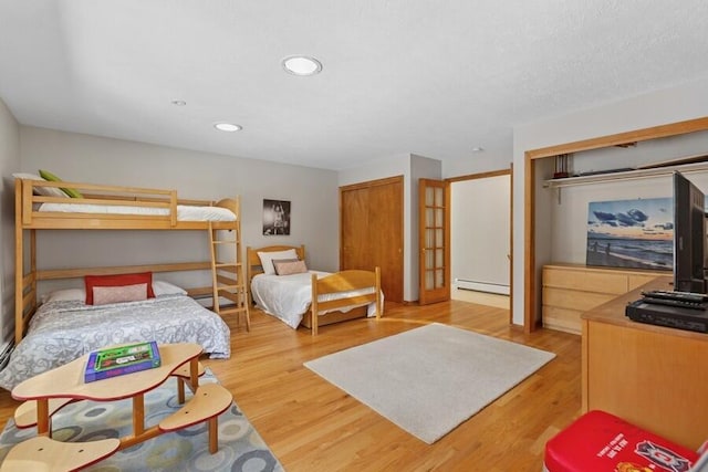 bedroom featuring wood finished floors, french doors, a baseboard heating unit, two closets, and recessed lighting