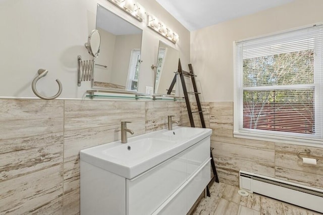 full bathroom featuring a baseboard radiator, a wainscoted wall, a sink, tile walls, and double vanity