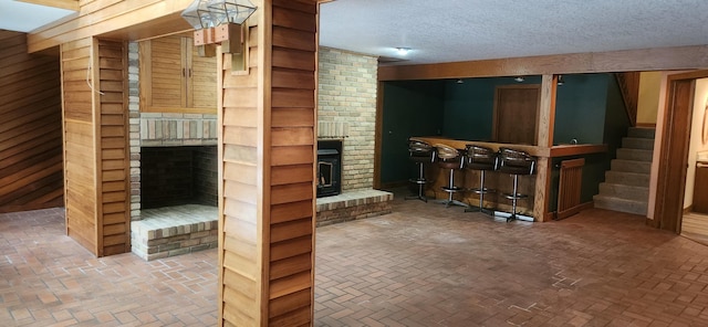 3075 Mineral Springs Trl, Mount Pleasant, MI 48858 - living room featuring a brick fireplace, stairs, a dry bar, brick flooring, and a textured ceiling