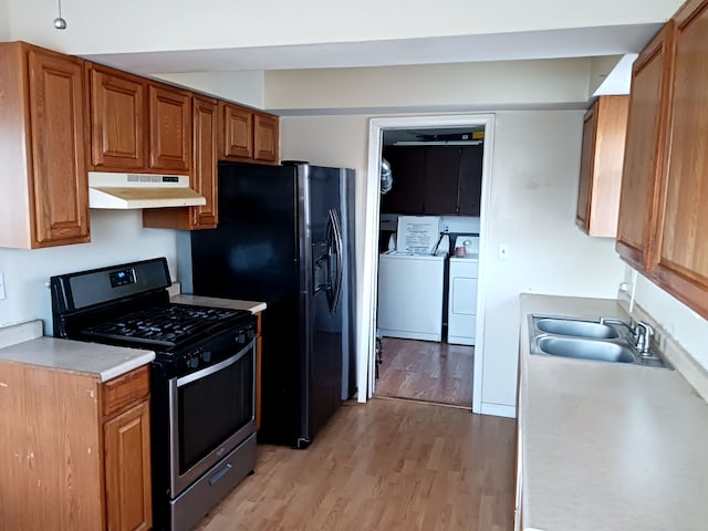 kitchen with light wood finished floors, under cabinet range hood, gas range, separate washer and dryer, and a sink