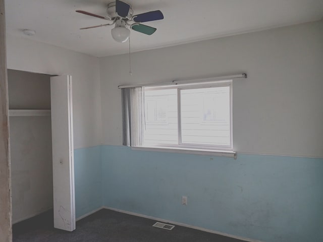 unfurnished bedroom with visible vents, a ceiling fan, and dark colored carpet