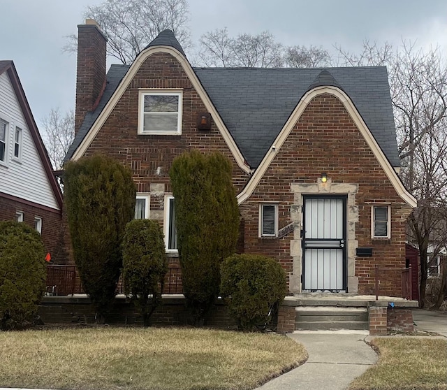 tudor house with brick siding, a chimney, and a front yard