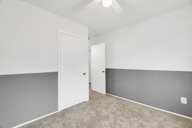 carpeted empty room with a ceiling fan and wainscoting