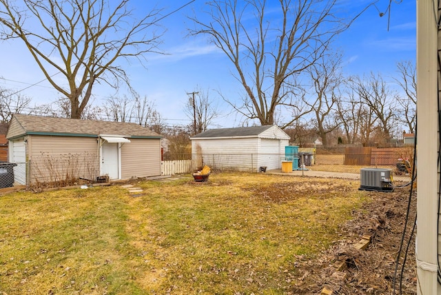 view of yard featuring central air condition unit, a detached garage, fence, and an outdoor structure