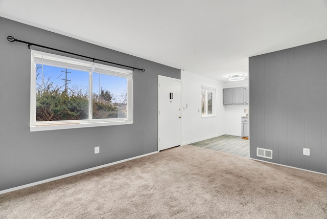 unfurnished living room featuring baseboards, visible vents, and light colored carpet