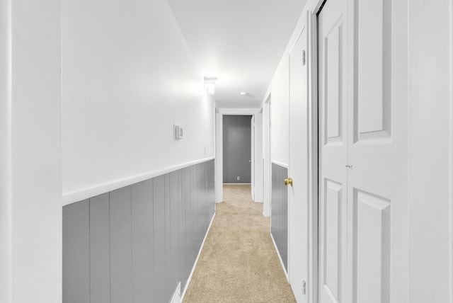 hall featuring a wainscoted wall and carpet flooring