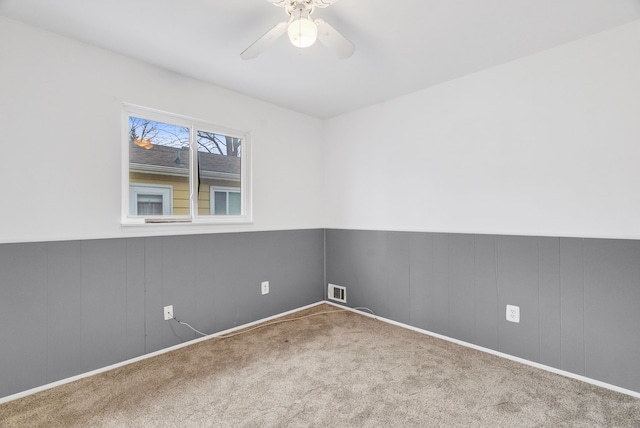 spare room with ceiling fan, a wainscoted wall, carpet flooring, and visible vents