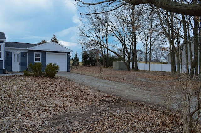 view of side of property with a garage, driveway, roof with shingles, and fence