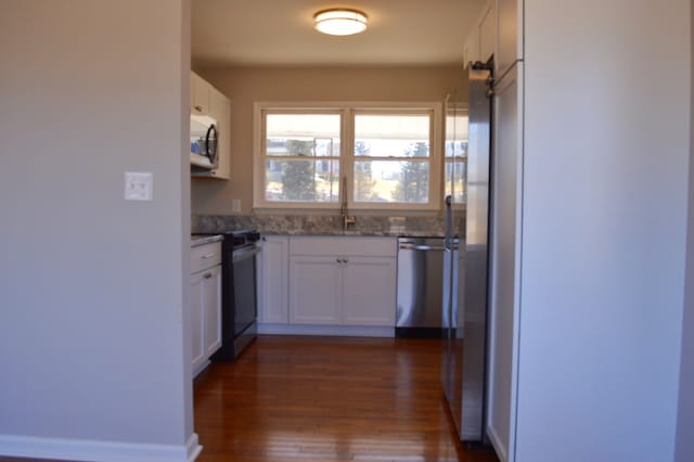 kitchen featuring white cabinets, dark wood-style flooring, light stone countertops, stainless steel appliances, and a sink