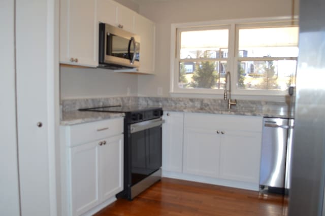 kitchen with stainless steel appliances, white cabinets, dark wood-type flooring, and light stone countertops