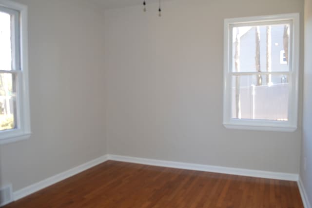 unfurnished room featuring dark wood-style floors, a wealth of natural light, and baseboards