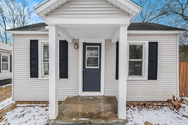 snow covered property entrance featuring roof with shingles