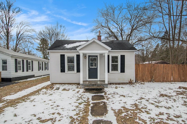 bungalow featuring a shingled roof, a chimney, and fence