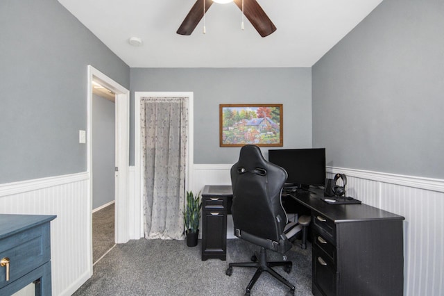 office featuring a wainscoted wall, dark carpet, and a ceiling fan