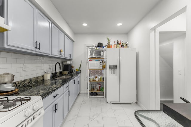 kitchen with tasteful backsplash, dark stone counters, marble finish floor, white appliances, and a sink